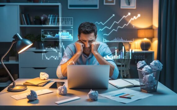 Male affiliate marketer reviewing failed plans and notes at his desk while analysing results on a laptop.